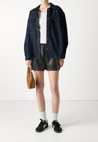 Jeansjacka med lös passform, två bröstfickor och metallknappar, kombinerad med svarta läderbyxor och svarta sneakers med vita detaljer.