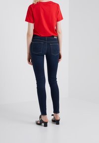 Vaqueros ajustados azules de mezclilla con una cintura de altura media, cinco bolsillos y costuras en contraste. Combinados con una camiseta de algodón roja y tacones negros.