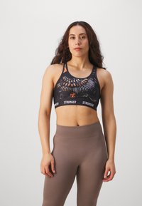 Reggiseno sportivo nero con design grafico colorato e logo "STRONGER" sulla fascia, abbinato a leggings marroni a vita alta con coste.