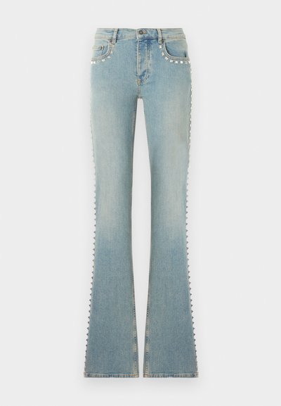 Ανοιχτό μπλε τζιν καμπάνα με ασημένια πυραμιδωτά καρφιά κατά μήκος των μπροστινών τσεπών και των εξωτερικών ραφών, κλείσιμο με κουμπί και φερμουάρ μπροστά.