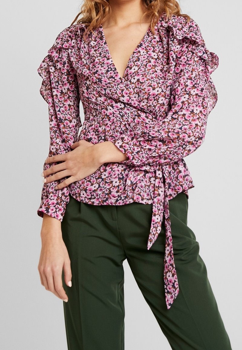 Blommig blus med rosa och vita blommor på mörk bakgrund. Har volangärmar, v-ringning och en knytning i midjan.