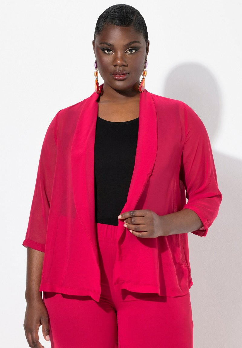Blazer rose transparent avec des manches 3/4, ouvert à l'avant, associé à un haut noir et un bas rose assorti. Design minimaliste, texture douce.