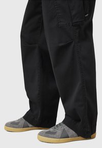 Pantaloni neri a gamba larga con una superficie morbida e tasche laterali, abbinati a sneakers grigie con una tomaia in suede e rete e suola in gomma.