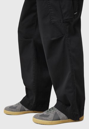 Black wide-leg pants with a smooth texture and side pockets, paired with gray sneakers featuring a suede and mesh upper and rubber sole.