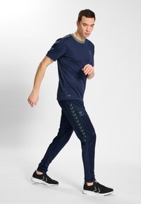 Completo sportivo blu con una maglietta a maniche corte con dettagli verdi e pantaloni abbinati che presentano un motivo verde lungo il lato.