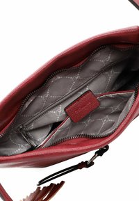 Interno di borsa in pelle rossa con fodera grigia a fantasia, una tasca con zip e due scomparti aperti, con cerniera e accessori neri.