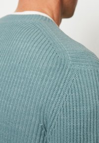 Helles blaues Strickpullover mit gerippter Textur und einem diagonalen Nahtdetail an der Schulter. Baumwollmischung, lässiges Design.
