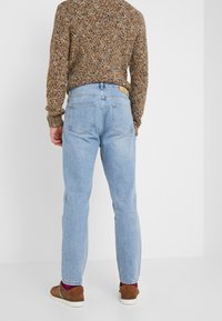Jeans de un azul claro con corte recto, diseño clásico de 5 bolsillos y una etiqueta de cuero en la parte posterior. Combinados con un suéter marrón texturizado y zapatos marrones.