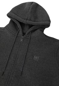 Sudadera gris con cremallera fabricada en tejido suave, que cuenta con capucha, cordones y un pequeño parche con logo. El diseño incluye una cremallera frontal y bolsillos.