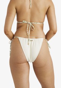 Krämfärgade bikiniunderdelar med justerbara snören i ett grönt och vitt mönstrat band. Har en jämn textur och elastiskt material.