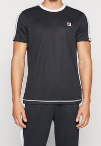 Svart atletisk t-shirt med vita accenter och rund halsringning, tillverkad av lättviktig tyg. Har en liten logotyp på bröstet och korta ärmar.