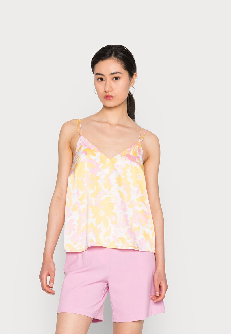 Camisola floral em amarelo e rosa, com alças finas e decote em V. Usada com calções rosa claros, exibindo um corte solto e tecido suave.