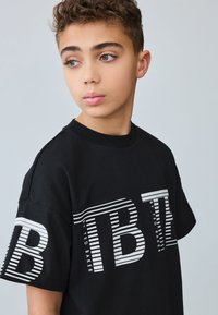 Sort bomulds-T-shirt med fedt, stribet grafisk tekst i hvid på forsiden, rund halsudskæring og korte ærmer.