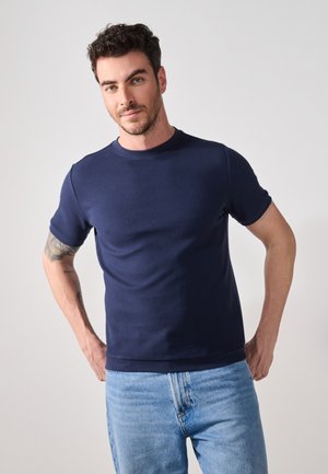 Navy blue ribbed t-shirt with a round neck and short sleeves, paired with light blue denim jeans. Simple design, textured fabric.