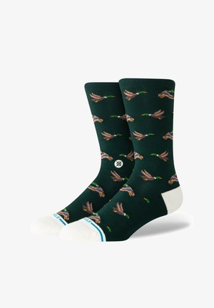 Calcetines verdes con un patrón repetido de patos voladores, con acentos en el puntera y talón reforzados en blanco, y una banda a rayas en la parte superior.