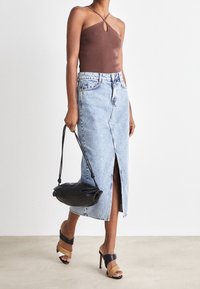 Hnědý žebrovaný halter top s detaily ve tvaru klíče, světle modrá džínsová midi sukně s předním rozparkem, černá kabelka a sandály s mnoha pásky.