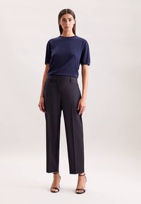 Marineblauw kortermig vest gecombineerd met een hoge taille donkere broek en zwarte sandalen met bandjes, met een gladde textuur en een op maat gemaakte pasvorm.