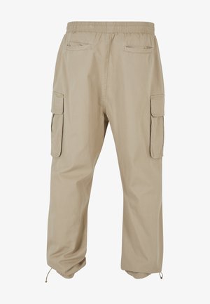 Beige cargo pants with elastic waistband, two side flap pockets, two back welt pockets, and adjustable drawstrings at the cuffs.