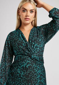 Grünes und schwarzes Leopardenmuster Kleid mit tiefem V-Ausschnitt, langen Ärmeln und einem verdrehten Frontdetail mit gerafftem Stoff an der Taille.