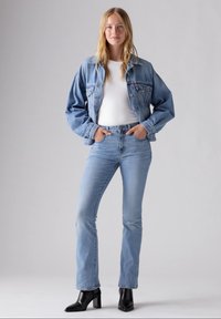 Light blue denim jacket with loose fit, white shirt underneath, and light blue jeans. Black heeled ankle boots complete the outfit.