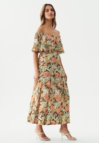 Bloemrijke maxi-jurk in groen, oranje en wit met off-the-shoulder ruffled mouwen, een aansluitend lijfje en een vloeiende rok.