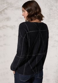Schwarzer Pullover aus weichem, strukturiertem Material mit weißer geometrischer Naht. Lockerer Schnitt und runder Ausschnitt. Lange Ärmel.