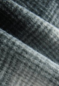 Tessuto grigio con una superficie morbida e texture presenta un sottile motivo a scacchi e fibre visibili, piegato a strati.