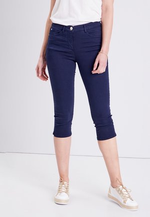 Jean cropped bleu marine en mélange de coton, avec une coupe ajustée, des poches arrière et des ourlets retroussés. Associés à des sneakers blancs et beiges.