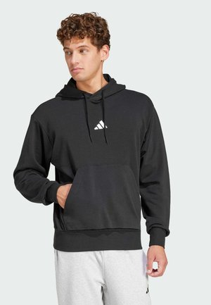 Zwarte hoodie met een voorzak in kangoeroestijl, een capuchon met koord en een wit logo op de borst. Zachte stof en geribbelde manchetten. Gecombineerd met grijze broek.