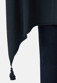 Ciemnoniebieska tkanina z ostrym brzegiem i frędzlami, wiszącymi nad ciemnoniebieskimi dżinsami na jasnym tle.