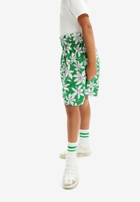 Gröna shorts med vitt blommönster, elastisk midja, kombinerat med vita strumpor med gröna ränder och genomskinliga sneakers.