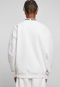 Hvid sweatshirt med løstsiddende pasform, der har en ribbet krave. Sort "STARTER" logo på bagsiden af halsudskæringen, glat tekstur.