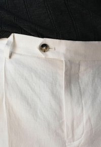 Nærbillede af hvide bukser med knaplukning i taljen og bæltestrop, kombineret med en sort tekstureret top, der er stukket ind.