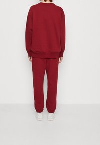 Conjunto de sudadera y pantalones jogger en burdeos, con un corte relajado, puños acanalados y dobladillos en los tobillos, todo ello con una suave textura de algodón.