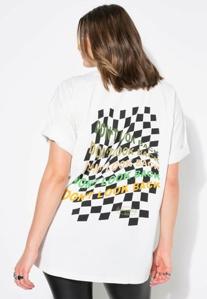 T-shirt blanc surdimensionné avec un motif à carreaux et un texte graphique en noir, vert et orange indiquant "NE REGARDE PAS EN ARRIÈRE". Tissu en coton doux.