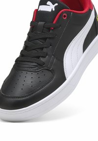 Sort lædersneaker med hvide accenter, rød indersål, perforeret tå, sorte snørebånd og en hvid gummisål. Puma-logo på tungen.