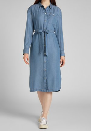 Abito camicia in denim con maniche lunghe, chiusura a bottoni frontale, cintura in vita e taschino sul petto. Il colore è azzurro chiaro con una texture liscia.