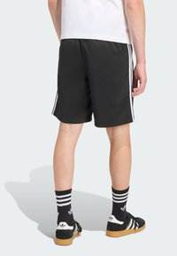 Čierne športové šortky majú po každej strane tri biele pruhy, vyrobené z hladkej textílie. Nosené s čiernymi ponožkami a teniskami.