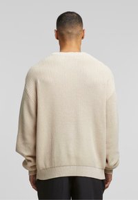 Beige striktrøje med et struktureret mønster, ribbede manchetter og kant. Løs pasform med en bred, rund udskæring. Bageste udsigt vist.