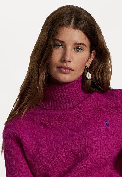Pulover magenta, cu guler înalt și model tricotat, având o margine ondulată. Are un mic detaliu cu logo albastru pe piept, fiind confecționat dintr-un material tricotat moale.