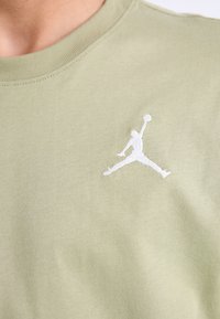 Lys grøn kortærmet T-shirt med ribbet halsudskæring, prydet med et hvidt broderet Jumpman-logo på venstre bryst. Blødt bomuldsstof.