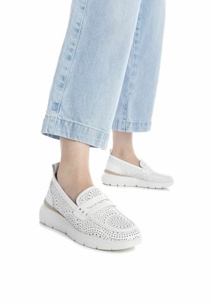 Sneakers bianchi senza lacci con design perforato, punta arrotondata, suola spessa e un accento beige chiaro vicino al tallone. Culotte in denim visibili sopra.