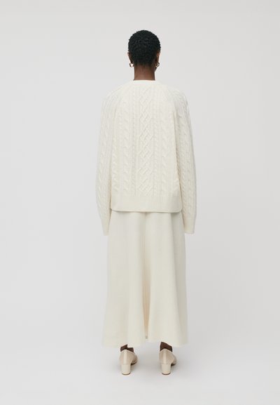 Grietos kabeliu megztinis, užsimestas ant derančios laisvai krintančios sijono, abu pagaminti iš minkštos, tekstūruotos vilnos, derinami su šviesiais, blokiniais kulnais.