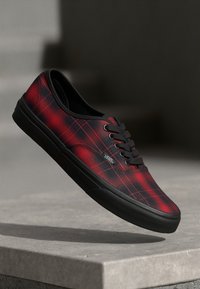 Zapatillas de lona a cuadros rojas y negras con suela de goma negra y cordones. Presenta el logo de Vans en el costado y un diseño de punta redonda.