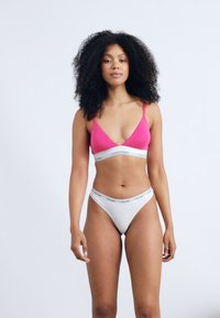 Rozā bralete ar plānām siksniņām un balts tanga apakšbikses ar elastīgu jostu, uz kuras ir "Calvin Klein" logo. Gluda auduma, minimālisma dizains.