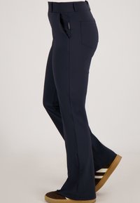 Marineblauwe slim-fit broek met achter- en zijzakken, gedragen met bruine sneakers met witte en zwarte strepen.