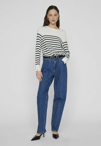 Suéter de manga larga a rayas en blanco y azul marino, combinado con jeans de mezclilla azules sueltos, cinturón negro y tacones negros puntiagudos.
