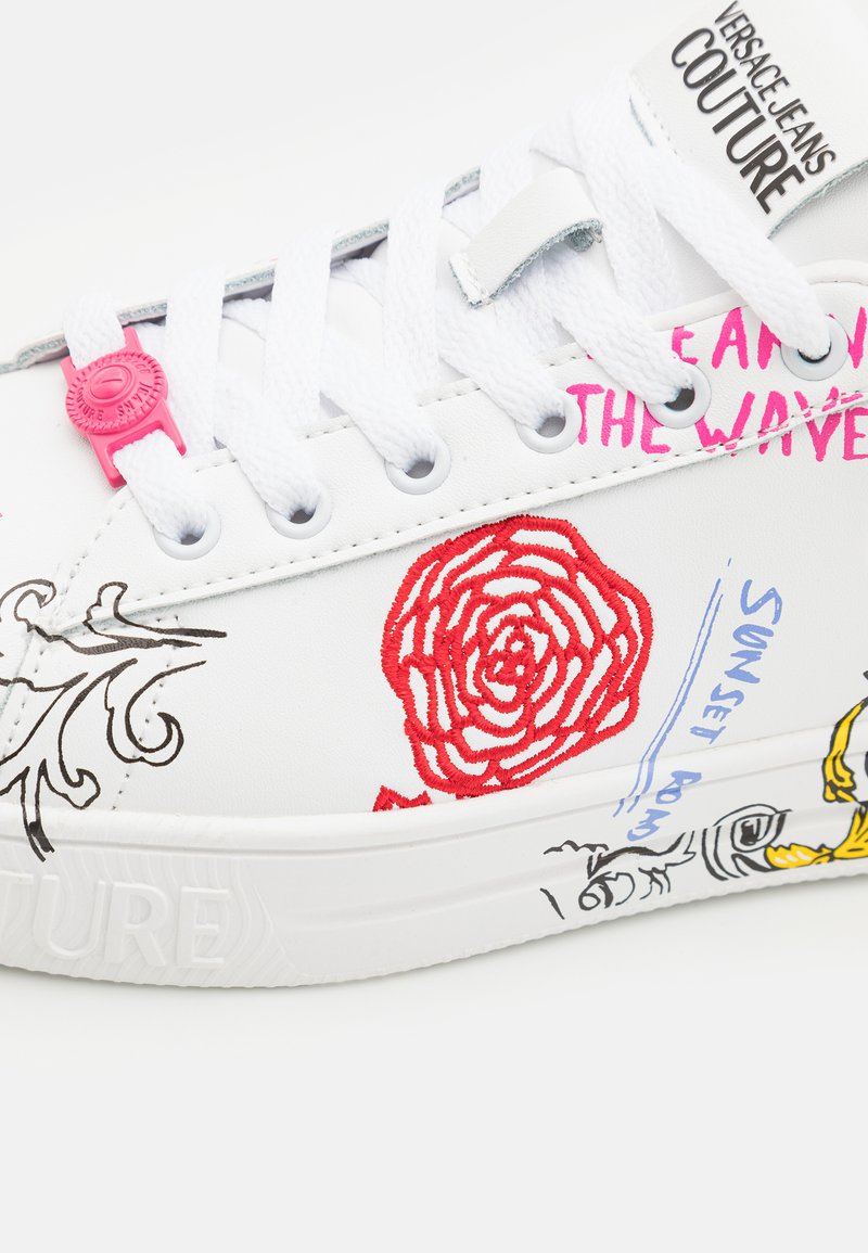 Sneaker bianca in tela con ricami floreali rossi e grafiche stampate in rosa e blu. Occhielli perforati e lacci bianchi.