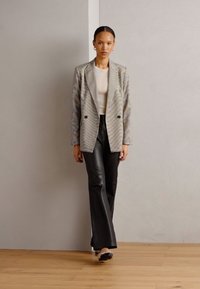 Blazer strutturato a righe multicolori, pantaloni in pelle nera e scarpe nere. Il blazer presenta un design doppiopetto e rever a punta.