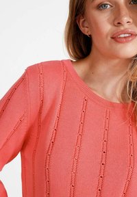 Korall színű kötött pulóver, kerek nyakkal, függőleges csíkos mintázattal, textúrált anyaggal és laza szabással.